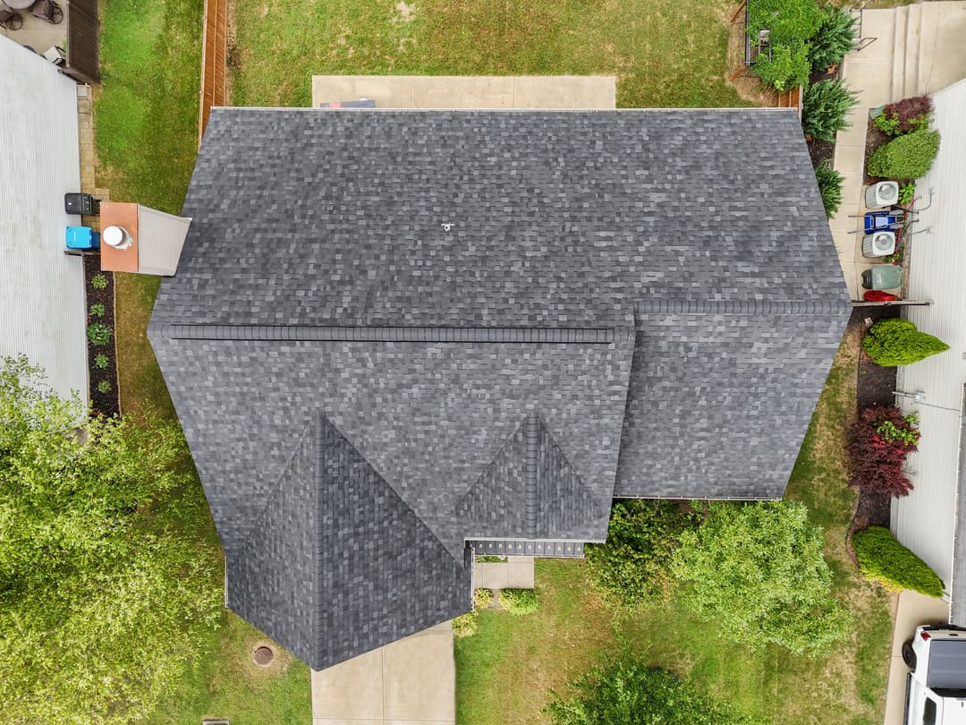 Aerial view of a residential roof with dark shingles and surrounding greenery.