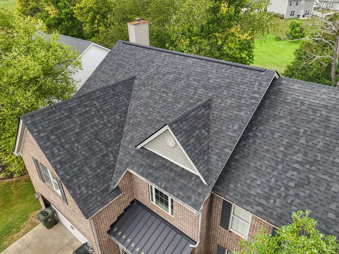 Aerial view of a modern house with a dark shingle roof and landscaped surroundings.
