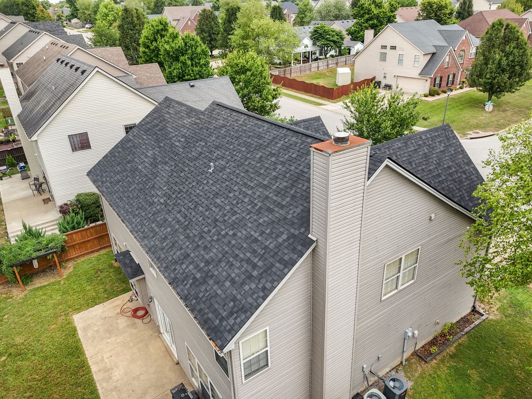 Aerial view of suburban home with gray shingles and well-maintained landscaping.