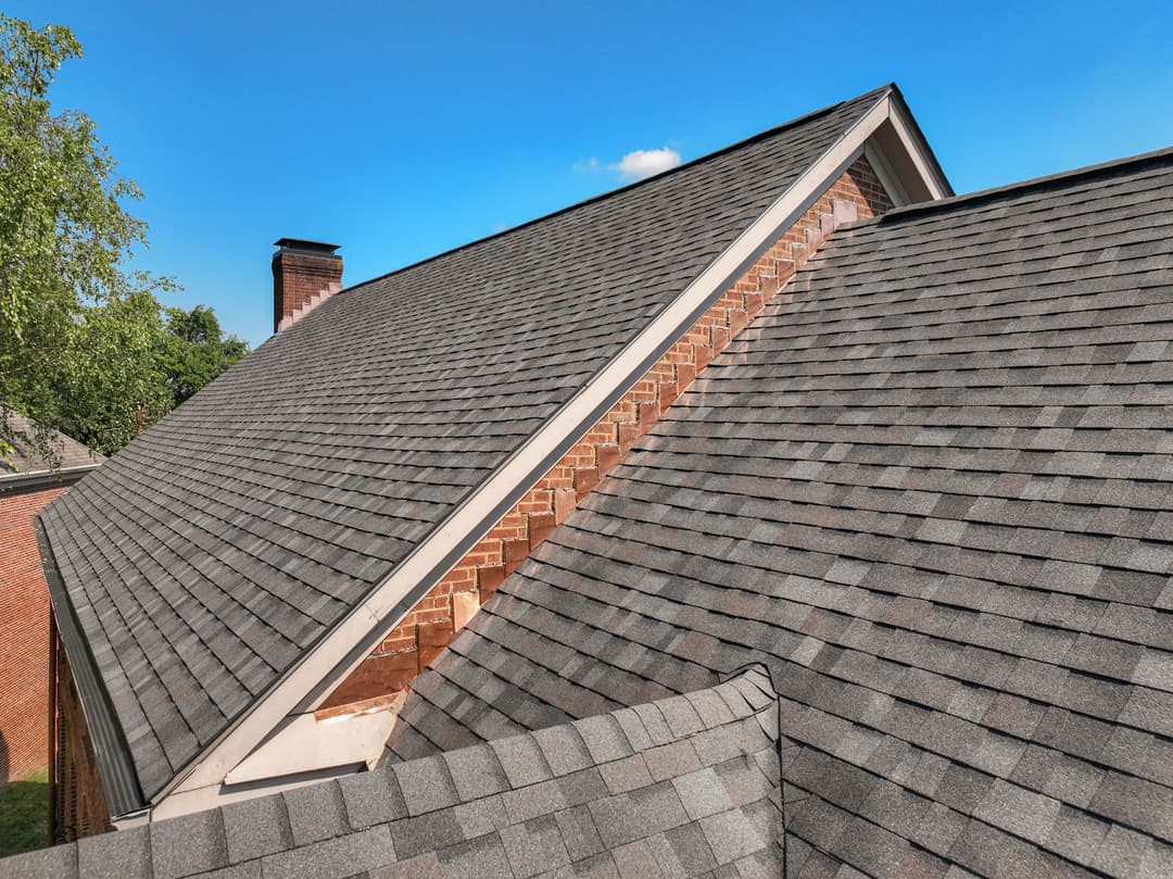 Roof shingles on a sloped roof with a brick chimney against a clear blue sky.