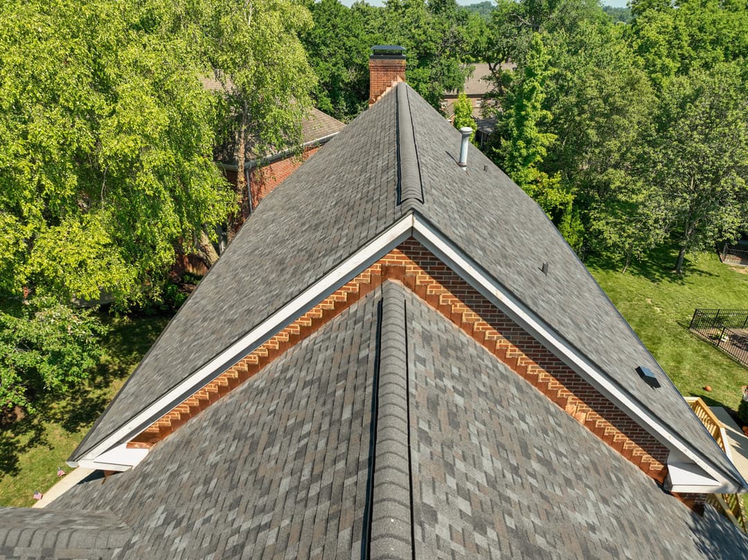 Aerial view of a well-maintained asphalt shingle roof on a residential home surrounded by trees.