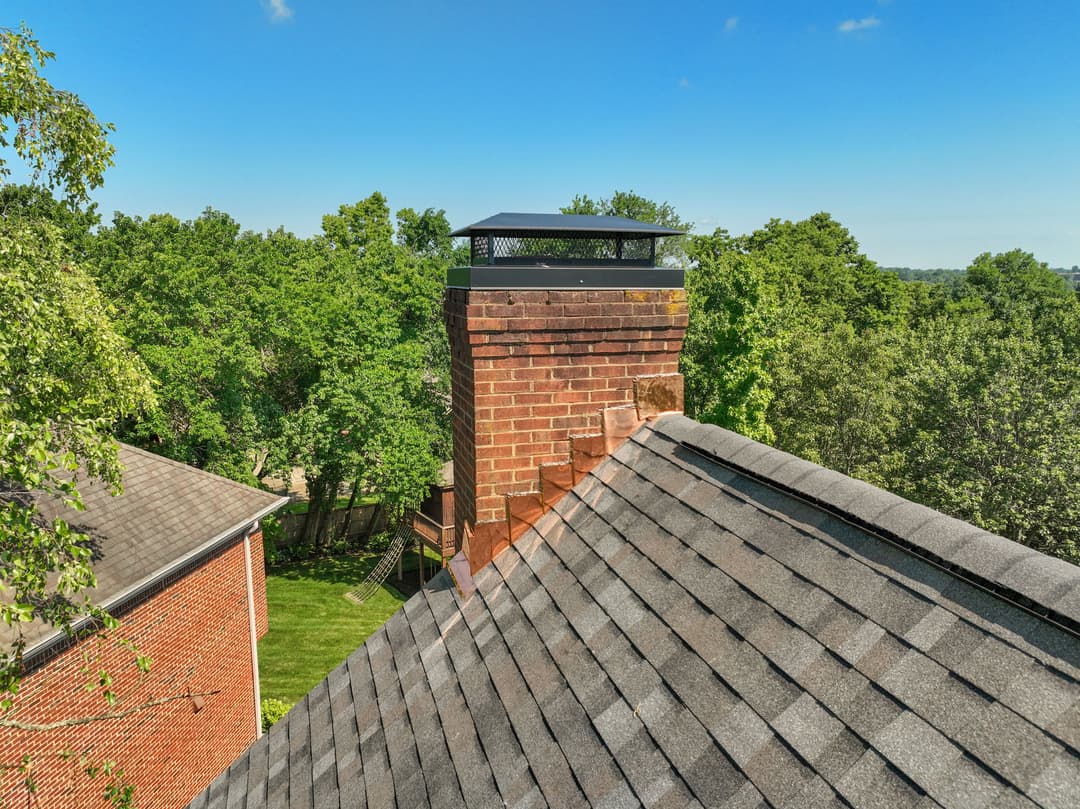 Chimney on a house roof surrounded by trees and clear blue sky.