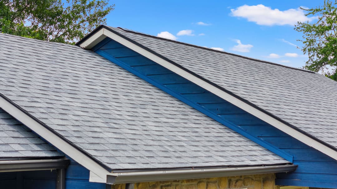 Blue house with a sloped gray shingle roof under a clear blue sky.