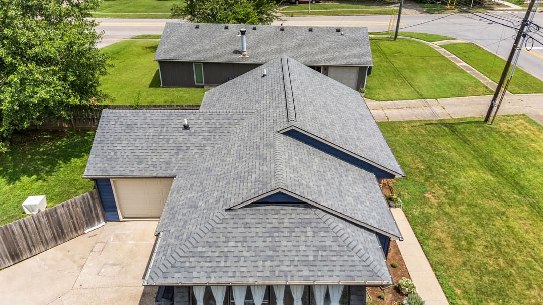 Aerial view of residential roofs and green lawn in a suburban neighborhood.