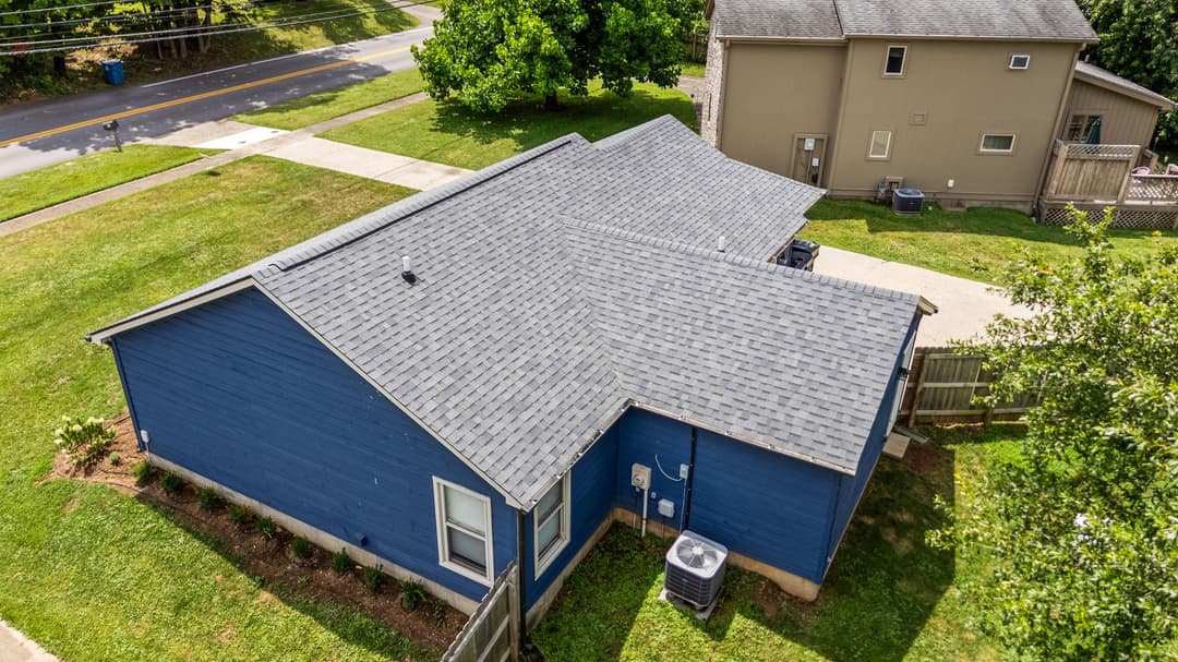 Aerial view of a blue house with a new roof and well-maintained landscaping.