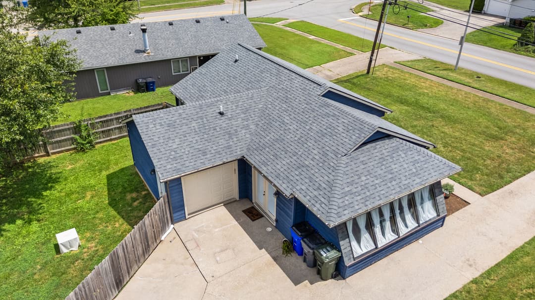 Aerial view of a blue house with a gray roof and landscaped yard on a suburban street.
