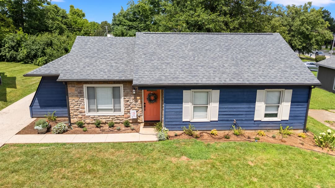 Modern blue house with stone accents, lush garden, and inviting orange front door.