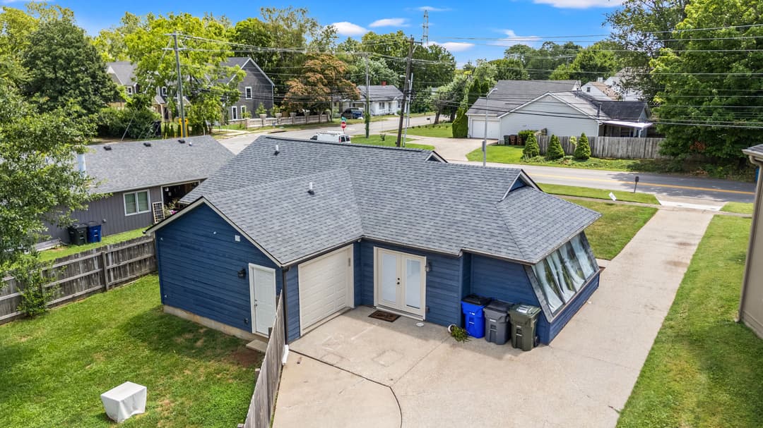 Aerial view of a blue house with a sunroom and driveway, surrounded by greenery.