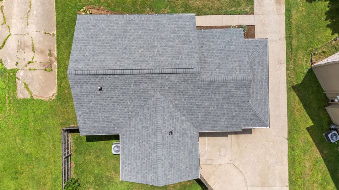 Aerial view of a residential roof with gray shingles and surrounding green grass.