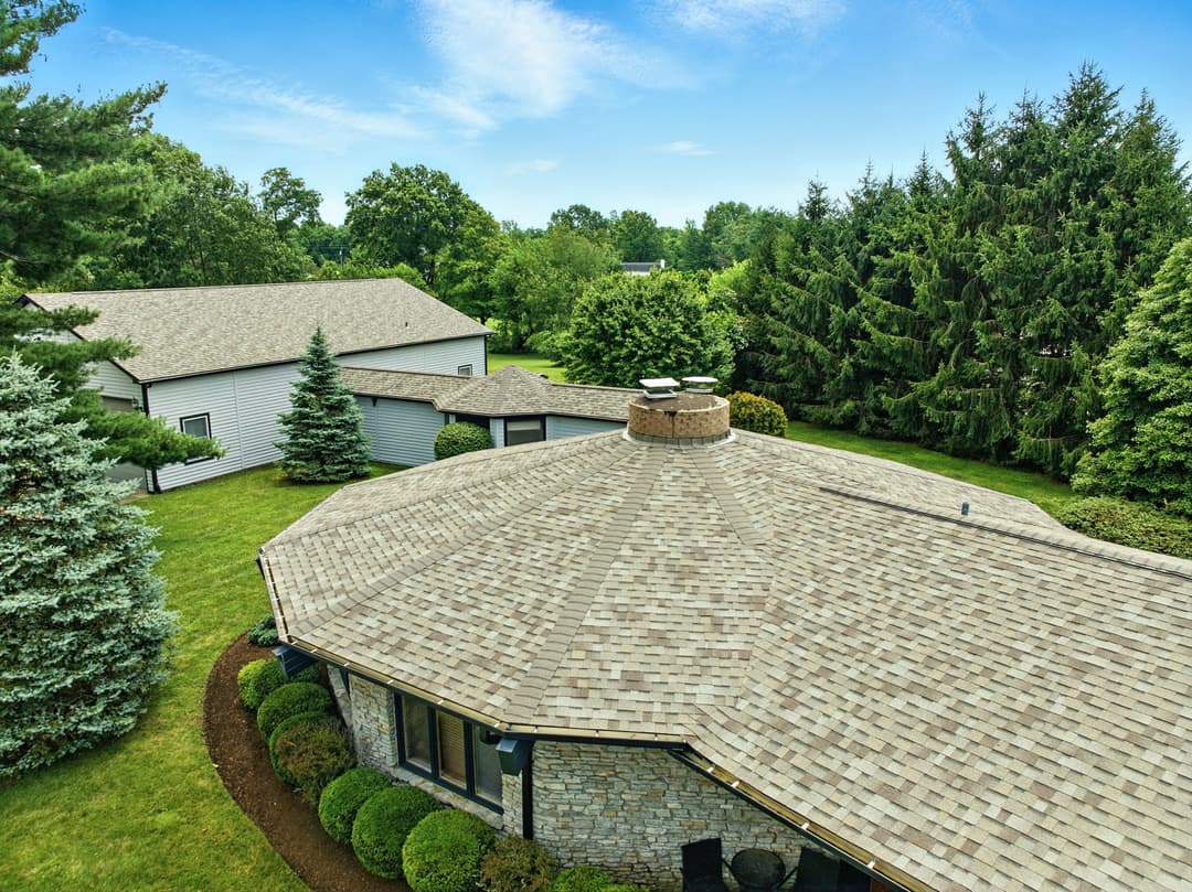 Aerial view of a home with a multi-sided roof and lush green landscaping surrounding it.