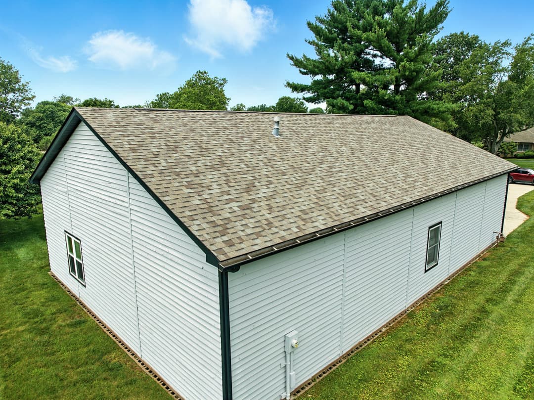 Aerial view of a well-maintained house with a gray shingle roof and lush green surroundings.