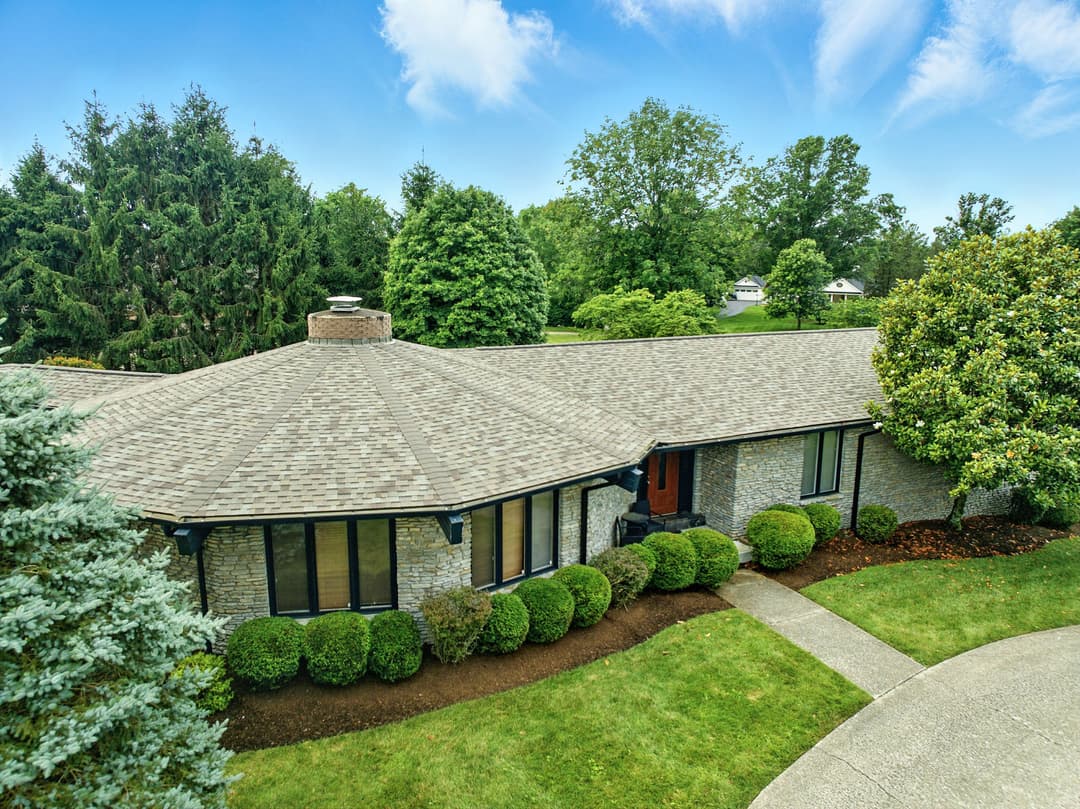 Spacious ranch-style home with lush landscaping and circular driveway under blue skies.