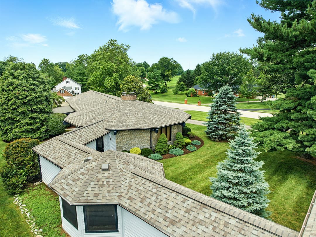 Aerial view of a landscaped home with a stone exterior and surrounding greenery.