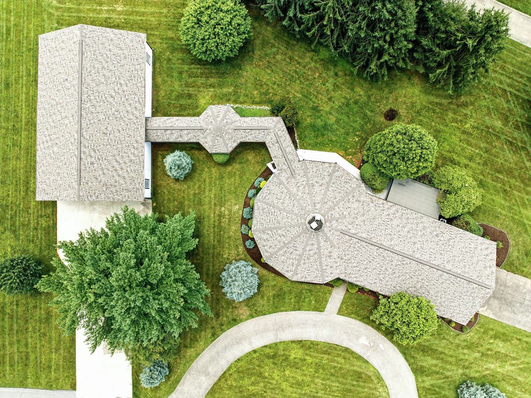 Aerial view of a landscaped property featuring a circular patio and adjacent homes.