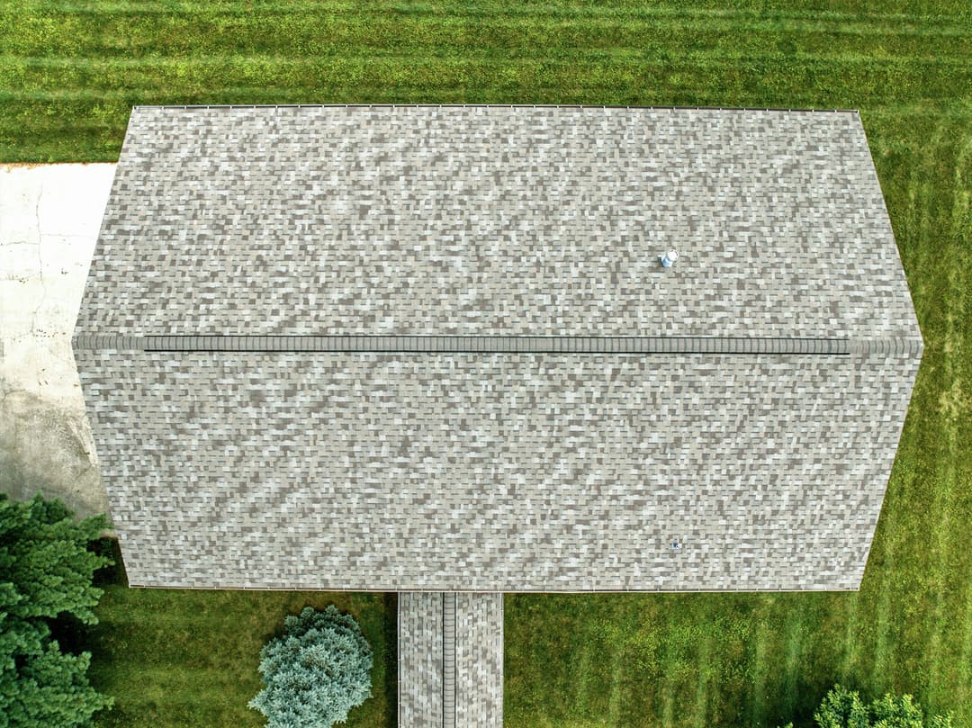 Aerial view of a gray shingle roof with green grass surrounding the house.